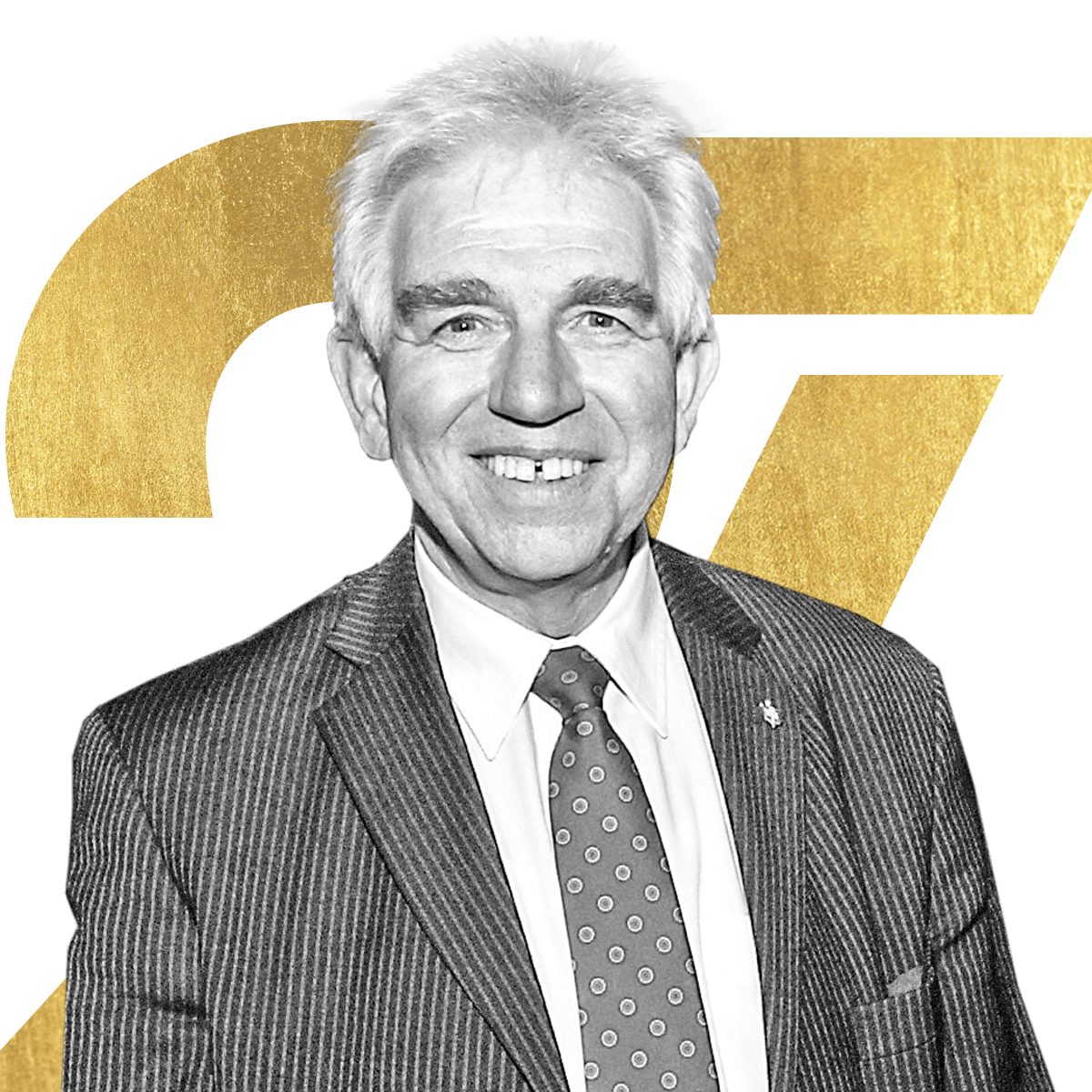 Ein lächelnder älterer Mann im Anzug und mit gepunkteter Krawatte steht vor einem großen goldenen ST auf weißem Hintergrund.